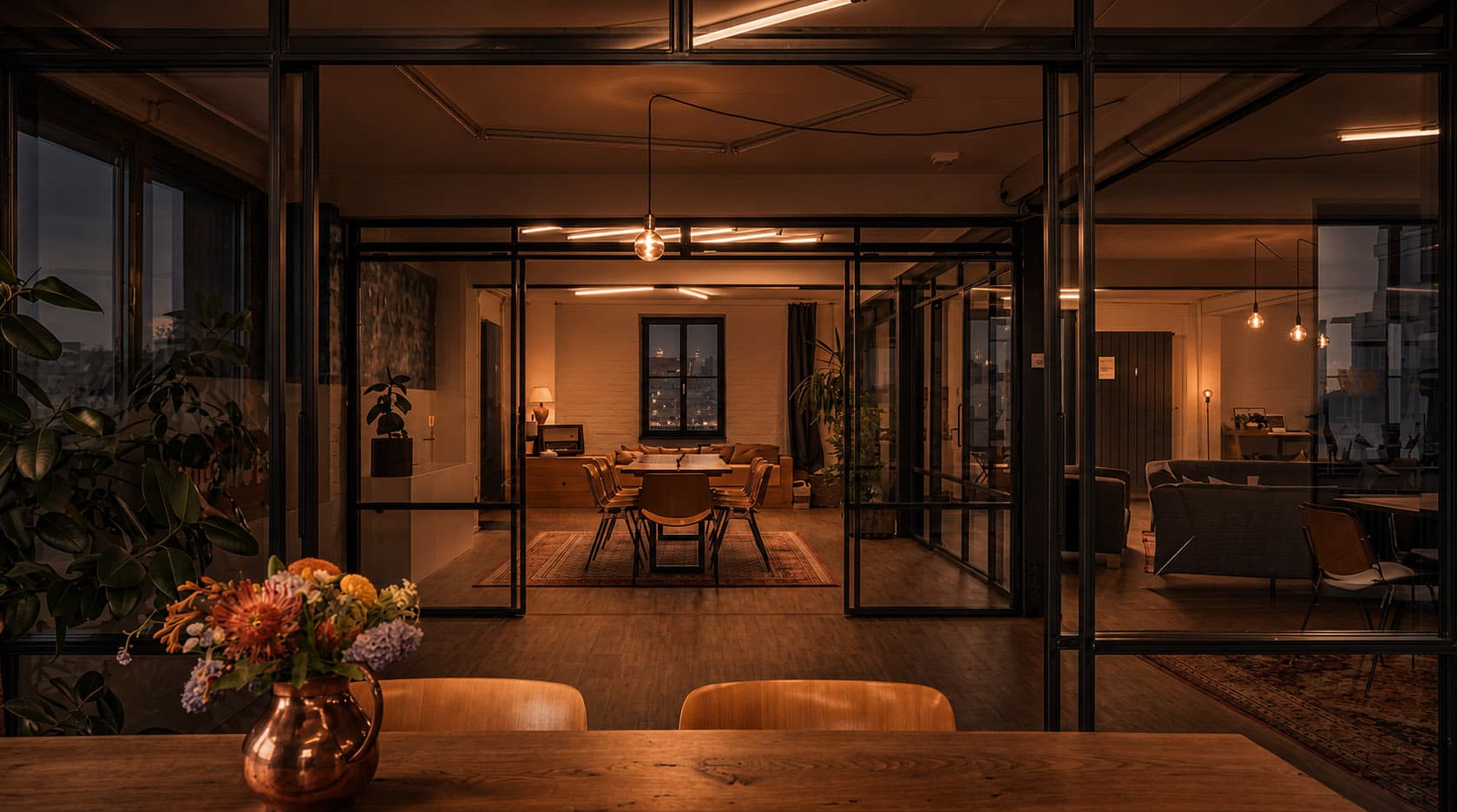 Industrial-Loft mit Glas-Trennwänden, langer Tafel und warmem Licht